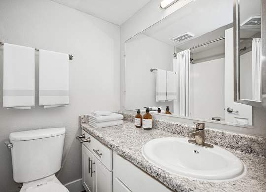 Model Bathroom with White Cabinets and Wood-Style Flooring at Stillwater Apartments located in Glendale, AZ.