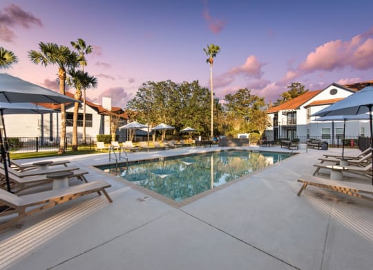 a swimming pool with lounge chairs and umbrellas at the resort with a building