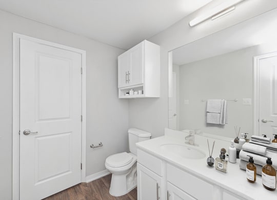 Model Bathroom with White Cabinets and Wood-Style Flooring at Hidden Creek Apartments located in Lewisville, TX.