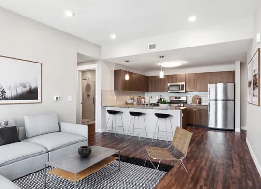 Model Living Room with Wood-Style Flooring and View of Kitchen at Seven Skies Apartments located in Sandy, UT.