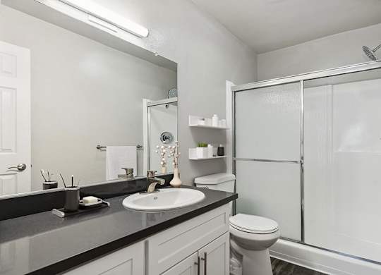 Model Bathroom with White Cabinets, Wood-Style Flooring and Shower at Madison Park Apartments located in Anaheim, CA.