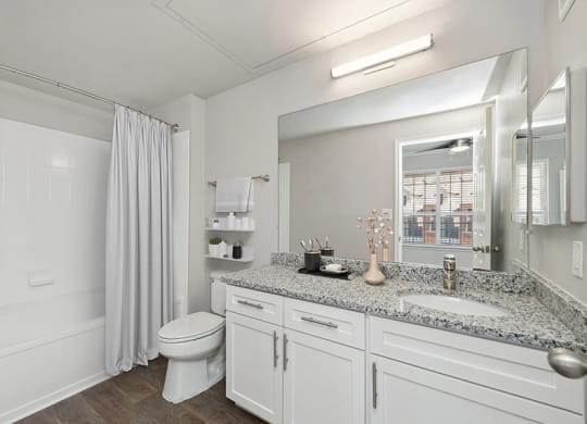 Model Bathroom with White Cabinets, Wood-Style Flooring and Shower/Tub at Chapel Hill Apartments in Lewisville, TX.