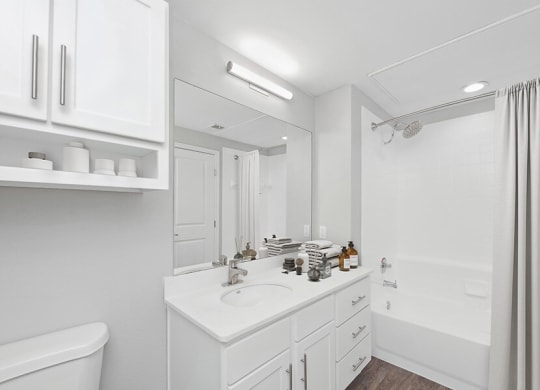 Model Bathroom with White Cabinets, Wood-Style Flooring & Shower/Tub at Hidden Creek Apartments located in Lewisville, TX.