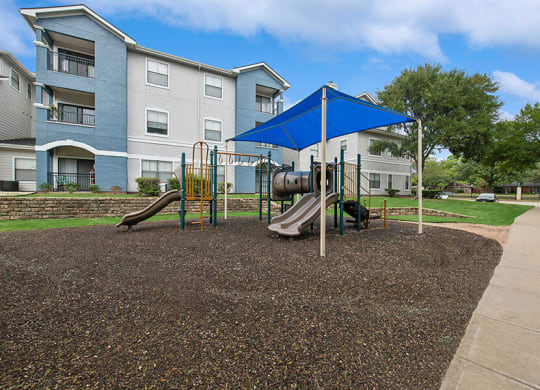 Community Playground with Slide and Blue Canopy at Hidden Creek Apartments located in Lewisville, TX.