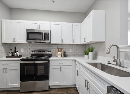 3-Bedroom Apartments in Lewisville, TX - Bridges at Oakbend - Kitchen With White Cabinets, Tile Backsplash, Stainless-Steel Appliances, Range With Microwave, And Double Sink With Sleek Faucet.