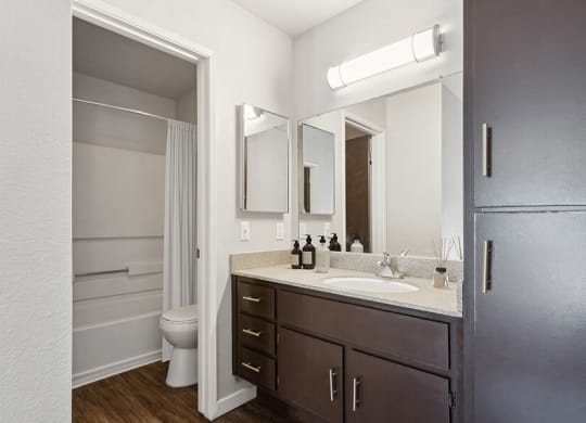 Model Bathroom with Dark Wood Cabinets, Wood-Style Flooring and Shower/Tub at Creek at 2645 Apartments located in Sacramento, CA.