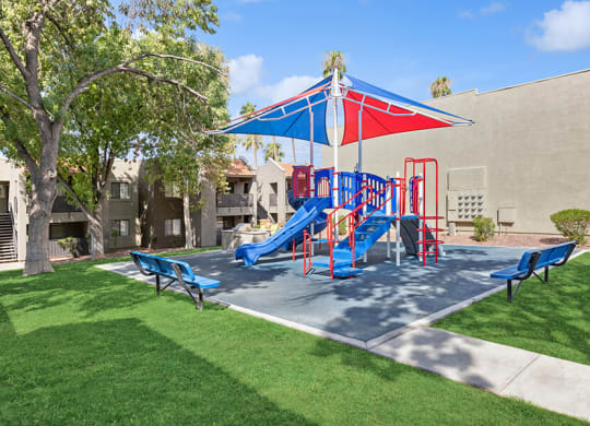 Community Playground with a Slide and Blue/Red Canopy at Saddle Ridge Apartments in Tucson, AZ.