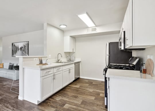 Model Kitchen with Wood-Style Flooring, White Cabinets and View of Living Room at Loma Vista Apartments in Las Vegas, NV.