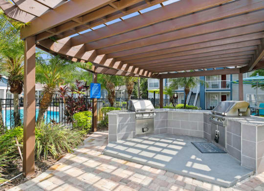 Pergola with two barbecue grills and a pool in the background at Retreat at Crosstown Apartments