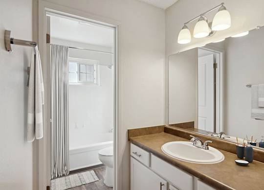 Model Bathroom with White Cabinets, Wood-Style Flooring and Shower/Tub at Los Gatos Landing Apartments located in San Jose, CA.
