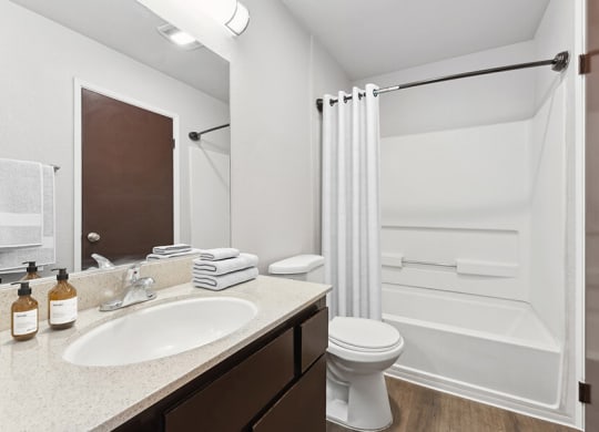 Model Bathroom with Dark Wood Cabinets, Wood-Style Flooring and Shower/Tub at Creek at 2645 Apartments located in Sacramento, CA.
