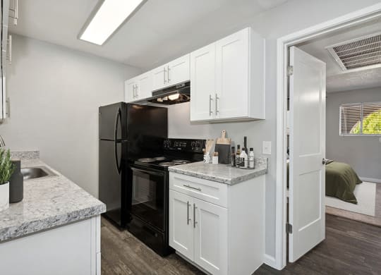 Model Kitchen with White Cabinets and Wood-Style Flooring with Bedroom Entrance at Stillwater Apartments in Glendale, AZ.