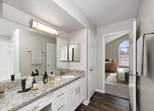 Model Bathroom with White Cabinets and Wood-Style Flooring at Hidden Creek Apartments in Lewisville, TX.