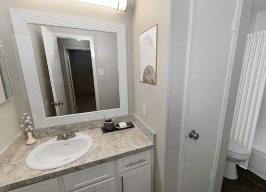 Model Bathroom with White Cabinets, Wood-Style Flooring and Shower/Tub at Dallas North Park Apartments in Dallas, TX.