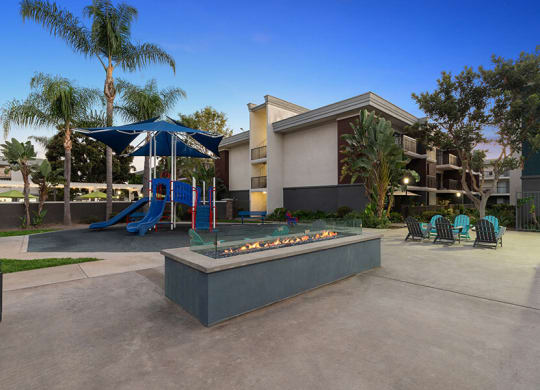Community Fire Pit Area with Lounge Furniture and View of Playground at Madison Park Apartments located in Anaheim, CA.