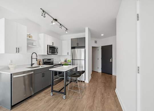 Model Kitchen with Dark Cabinets, Wood-Style Flooring and View of Living Room at Stella Apartments located in New Carrollton, MD.