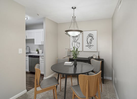 Model dining area with a table and chairs and kitchen in the background  at Stone Ends apartments in Stoughton, MA