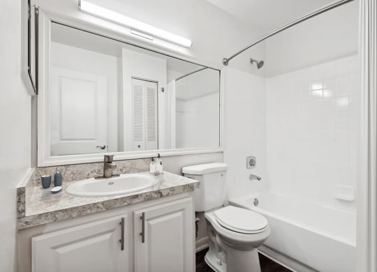 Model Bathroom with Wood-Style Flooring, White Cabinets & Shower/Tub at Rosehill Preserve Apartments located in Orlando, FL.