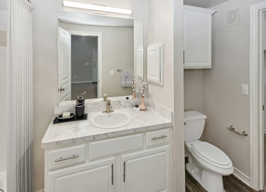 Model Bathroom with White Cabinets and Wood-Style Flooring at Belmont at Duck Creek Apartments in Garland, TX.