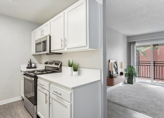 Model Kitchen with White Cabinets, Wood-Style Flooring and Living Room View at The Archer Apartments in Sacramento, CA.