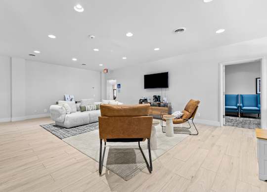 A living room with a white couch, a brown chair, and a television on the wall.