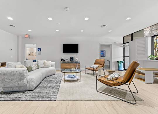 A living room with a grey sofa, a brown chair, and a TV mounted on the wall.