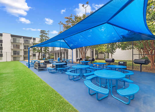 A blue canopy covers a picnic area with tables and benches.