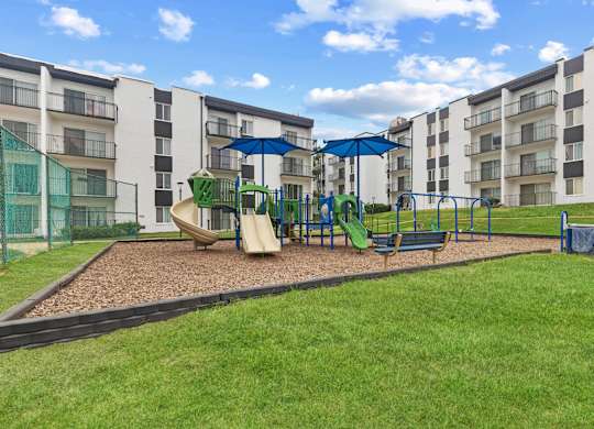 A playground with a green slide and a blue umbrella.