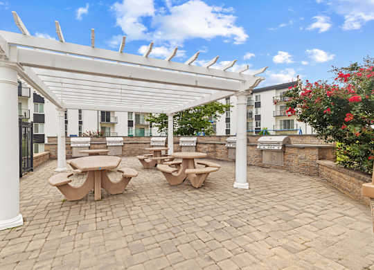 A white pergola with benches and tables is set up on a brick patio.
