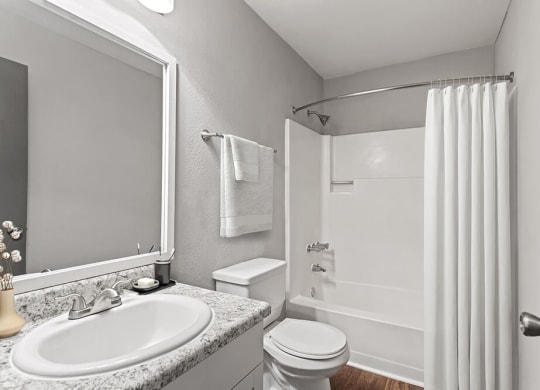 Model Bathroom with White Cabinets, Wood-Style Flooring and Shower/Tub at Corners at 1700 Apartments in Atlanta, GA.