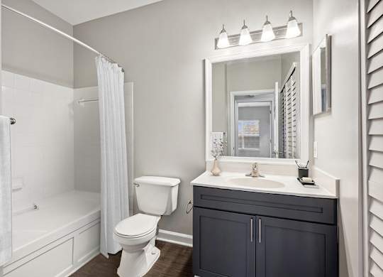 Model Bathroom with Dark Wood Cabinets and Wood-Style Flooring at Dulles Green Apartments located in Herndon, VA.