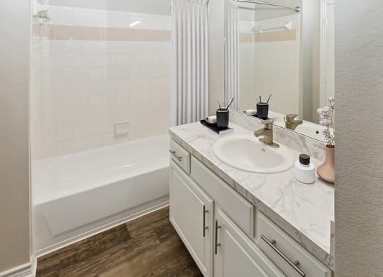 Model Bathroom with White Cabinets and Wood-Style Flooring at Belmont at Duck Creek Apartments in Garland, TX.