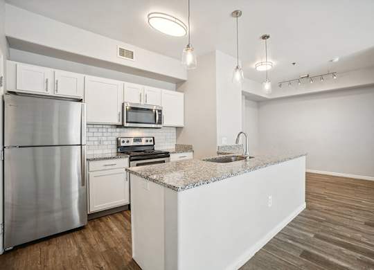 Model Kitchen with Wood-Style Flooring, White Cabinets, and Stainless-Steel Appliances at Altitude on Fifth Apartments located in Salt Lake City, UT.