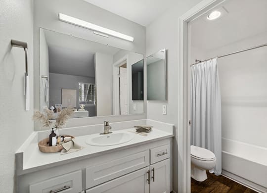 Model Bathroom with White Cabinets, Wood-Style Flooring and Shower/Tub at Central Flats Apartments in Kent, WA.
