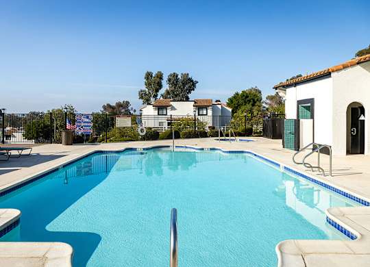 A swimming pool in a residential area with a house and trees in the background.