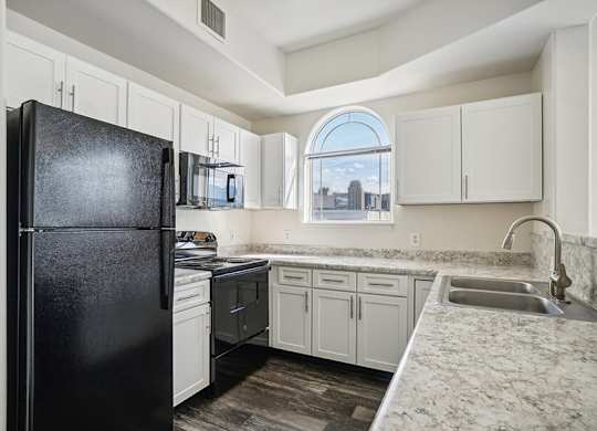 Model Kitchen with Wood-Style Flooring, White Cabinets, and Black Appliances at Altitude on Fifth Apartments located in Salt Lake City, UT.