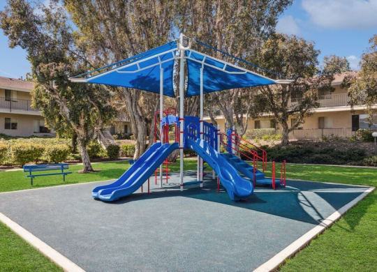 Community Playground with Two Slides and a Blue Canopy at Forest Park Apartments in El Cajon, CA.