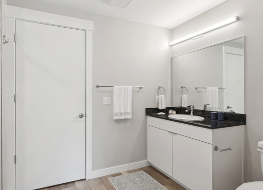 Model Bathroom with Wood-Style Flooring, White Cabinets & Shower/Tub at Seven Skies Apartments located in Sandy, UT.