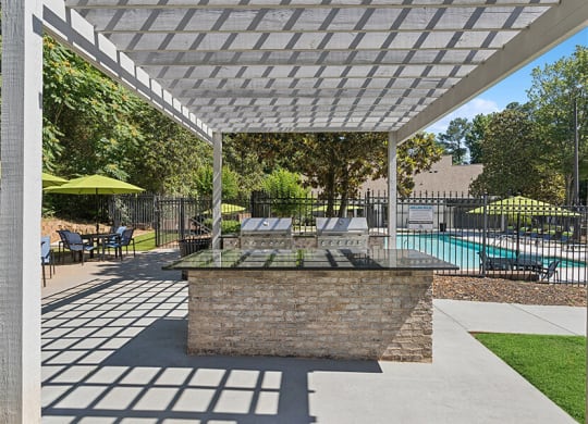 Outdoor BBQ Area with Canopy and View of Swimming Pool at Retreat at Stonecrest Apartments located in Lithonia, GA.