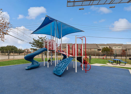 One-Bedroom Apartments in Lewisville, TX - Bridges at Oakbend - Community Playground With Slides, Climbing Structure, Shade Canopy, Picnic Tables On Soft Surface.