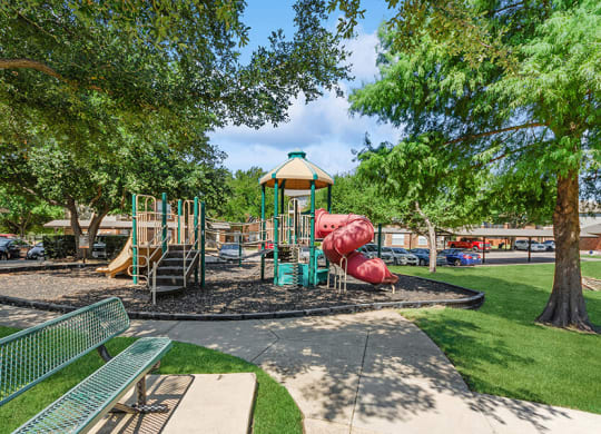Community Playground with Two Slides and Bench Area at Belmont at Duck Creek Apartments in Garland, TX.