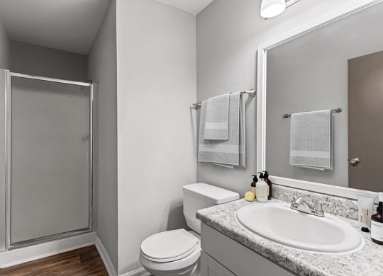 Model Bathroom with White Cabinets, Wood-Style Flooring and Standing Shower at Corners at 1700 Apartments in Atlanta, GA.