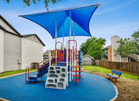 a playground with a swing set and a blue umbrella