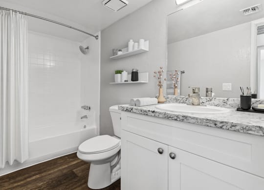 Model Bathroom with White Cabinets, Wood-Style Flooring and Tub/Shower at Tanque Verde Apartments located in Tucson, AZ.
