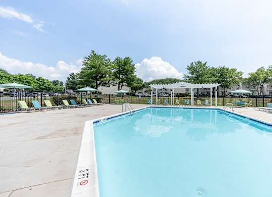 A large outdoor swimming pool with a white fence and trees in the background.