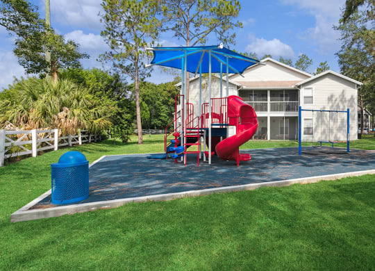 Community playground with a red slide and sun cover at Retreat at Crosstown Apartments