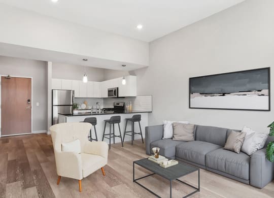 Model Living Room with Wood-Style Flooring and View of Kitchen at Seven Skies Apartments located in Sandy, UT.