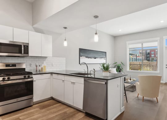 Model Kitchen with Wood-Style Flooring, White Cabinets and View of Living Room with Patio Accessibility at Seven Skies Apartments located in Sandy, UT.