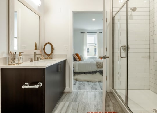 Model bathroom with a shower and a sink and a bedroom