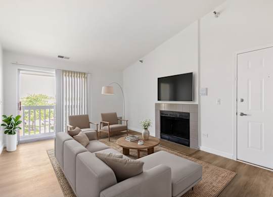 Model living room with a grey sofa, a wooden coffee table, a fireplace, and a sliding glass door leading to a balcony.
